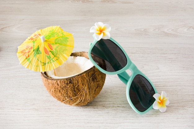 Noce di cocco ed occhiali da sole sulla tavola di legno bianca