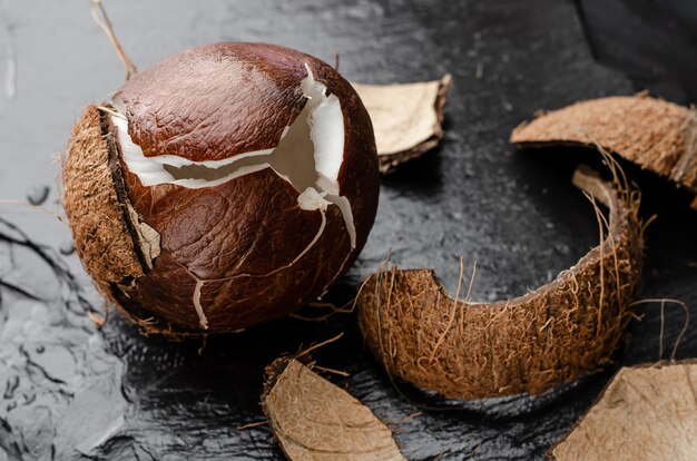 Noce di cocco matura rotta sul fondo nero della pietra dell'ardesia.