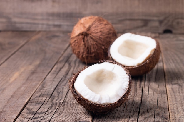 Noce di cocco tagliata a metà matura con foglie verdi su fondo di legno.