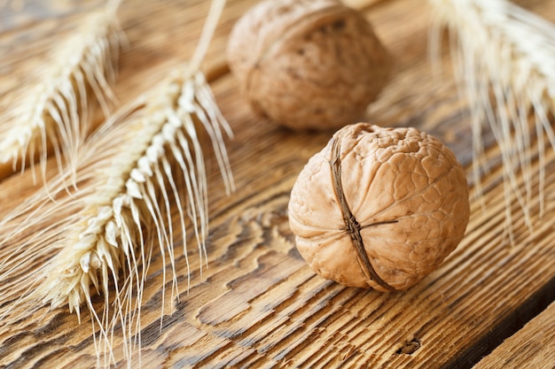 Noci del primo piano e spiga di grano sulla vecchia tavola di legno. Profondità di campo. Focus su una noce anteriore.