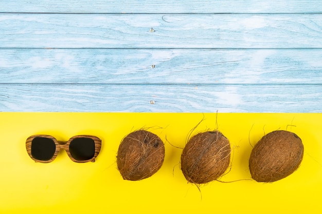 Noci di cocco e occhiali da sole in bugie su uno sfondo di legno blu e uno sfondo giallo