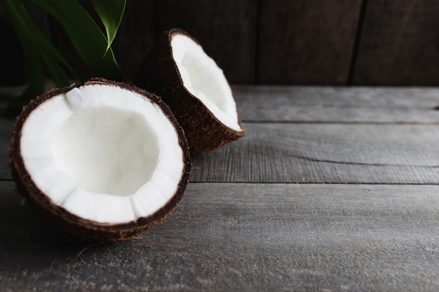 Noci di cocco rotte su fondo di legno grigio con foglia di palma. Polpa di cocco bianca. Foto di alta qualità