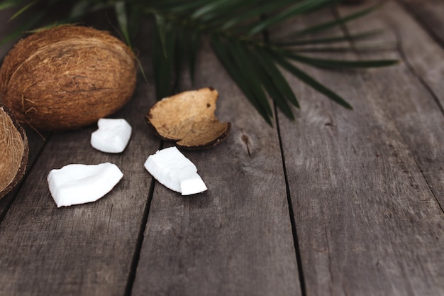 Noci di cocco rotte su fondo di legno grigio con foglia di palma. Polpa di cocco bianca.