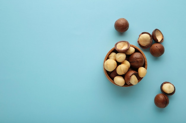 Noci di macadamia sbucciate in ciotola di legno su fondo blu