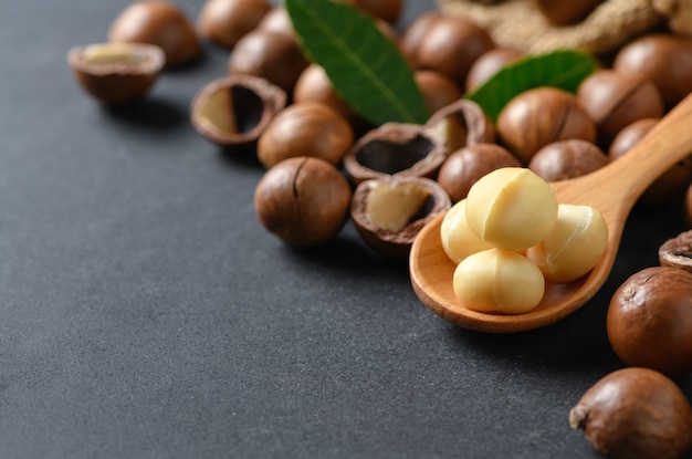 Noci di macadamia sul cucchiaio di legno sulla pietra nera