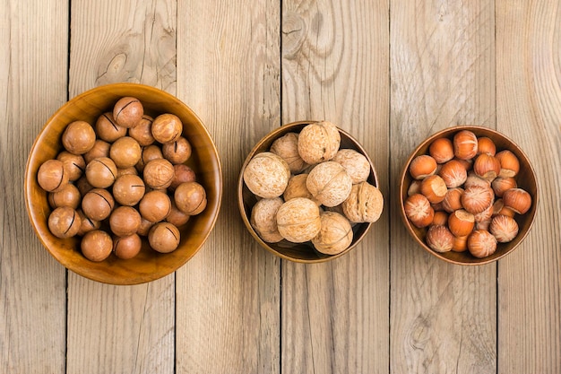 Noci di noce di macadamia organiche naturali in ciotola di legno su fondo di legno