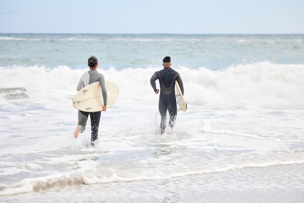 Noi apparteniamo all'oceano Foto di una coppia irriconoscibile che corre in acqua con le tavole da surf in spiaggia