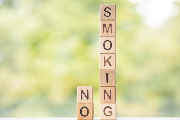 Non fumare è scritto su cubi di legno su uno sfondo verde estivo Primo piano di elementi in legno