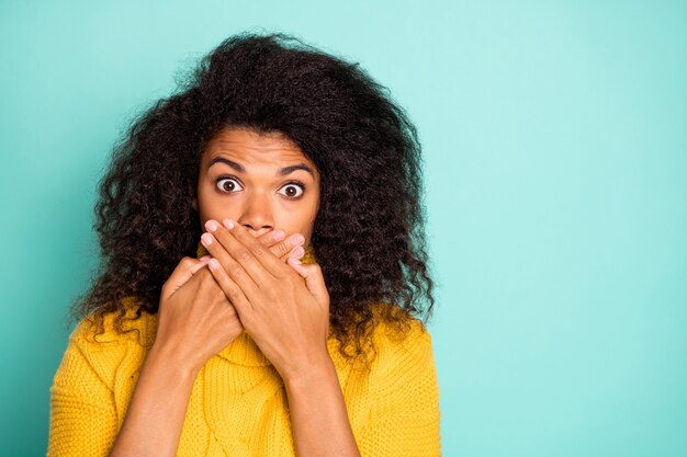 Non ho detto una parola! La foto del primo piano della signora piuttosto nervosa della pelle scura nello stupore che nasconde la bocca che tiene le mani vicino alle labbra indossa il ponticello lavorato a maglia giallo isolato la parete di colore blu verde acqua