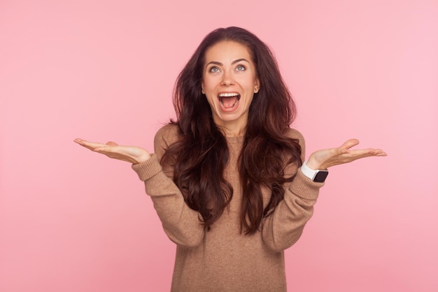 Non ho idea Ritratto di giovane donna eccitata e felice con i capelli ondulati bruna che scrolla le spalle le spalle perplesso gesticolando Non so chi se ne frega, quindi cosa girato in studio isolato su sfondo rosa