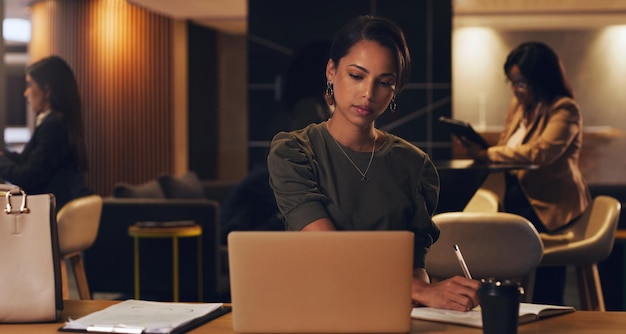 Non perde mai la dedizione Scatto di una giovane donna d'affari che scrive note mentre lavora su un laptop in un ufficio di notte