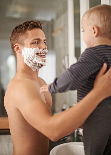 Non puoi ancora raderti piccolo uomo Inquadratura ritagliata di un uomo che tiene in braccio il suo bambino mentre si rade nel suo bagno