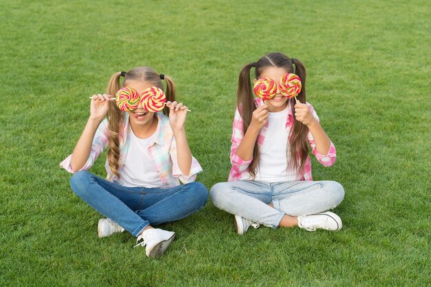 Non solo dolci ma bellissime da guardare Bambine con sguardo dolce sull'erba verde Bambini felici si coprono gli occhi con le caramelle Dolci Dolciumi Dolciumi La vita è dolce goditela di tutto