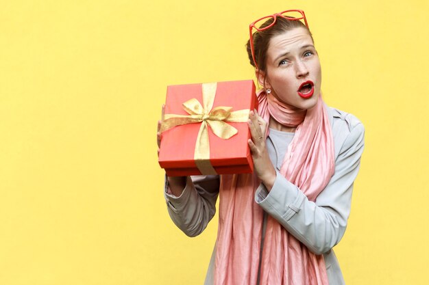 Non sopporto, è mio! Giocosamente giovane ragazza adulta con scatola regalo. Isolato su sfondo giallo, girato in studio