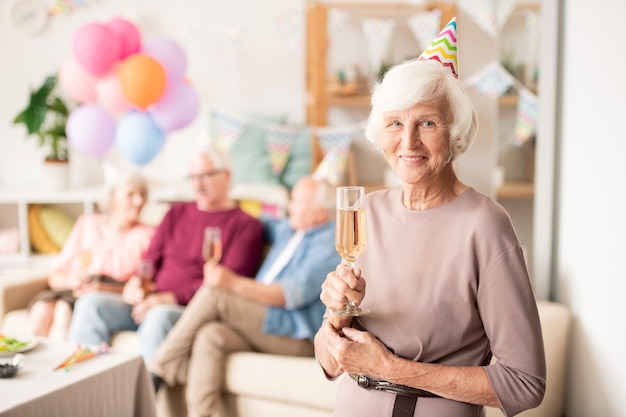 Nonna allegra in protezione di compleanno che tiene flauto di champagne