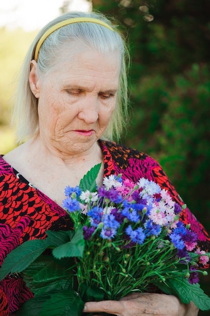 Nonna anziana con un mazzo di fiori nel parco.