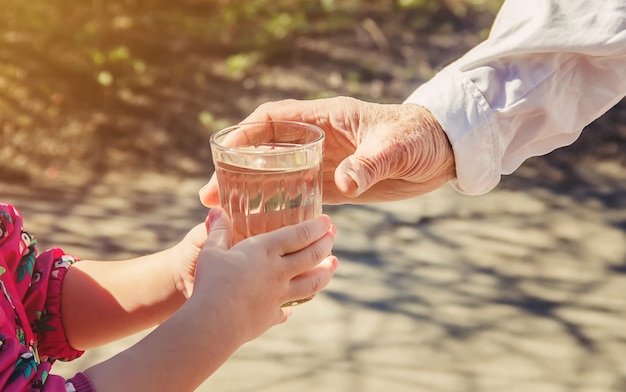 Nonna che dà un bicchiere di acqua pulita a un bambino. Messa a fuoco selettiva