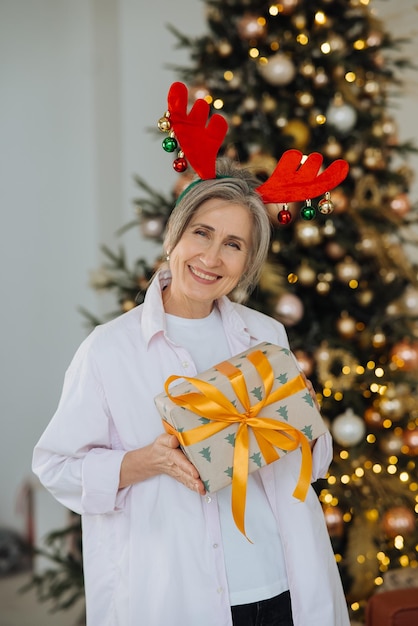 Nonna che indossa il cappello di Natale dei cervi Regalo di Natale in mano