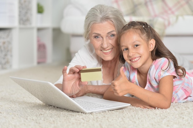 Nonna e nipote sdraiate sul pavimento e utilizzando il laptop o