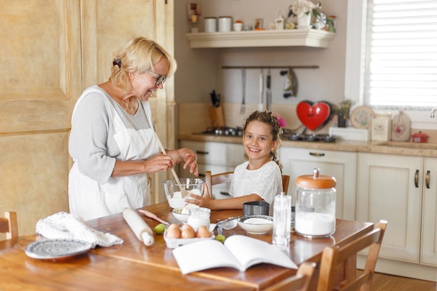 Nonna e nipotina adorabili si preparano insieme in cucina, con gli ingredienti in tavola.