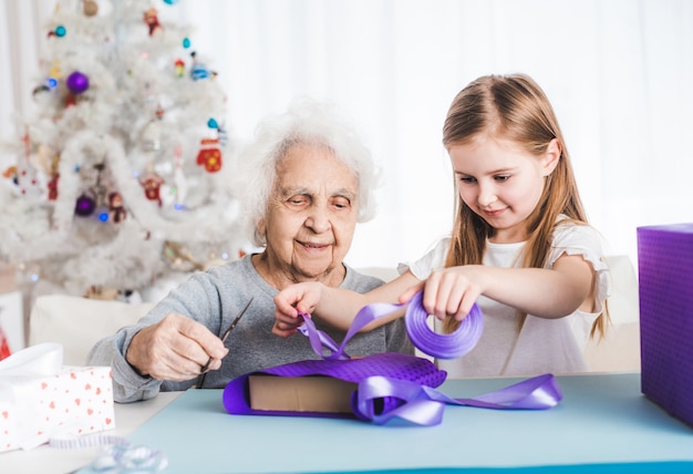 Nonna sorridente con la piccola nipote che decora insieme i regali