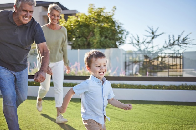 Nonni di famiglia e corsa con il bambino in giardino per una salute felice e amore insieme Cura della motivazione e l'estate con coppia di anziani e bambini sull'erba per il sorriso giovanile e il gioco nel quartiere