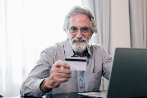 Nonno anziano in buona salute che utilizza il computer portatile e paga denaro con carta di credito per lo shopping online