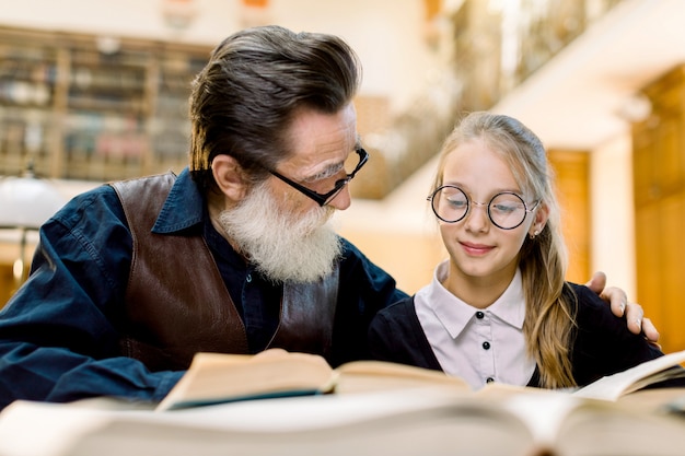 nonno barbuto uomo anziano e piccolo libro di lettura nipote carino insieme, seduti al tavolo nella vecchia biblioteca d'epoca