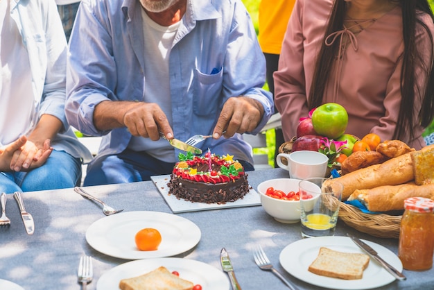 Nonno con la torta di compleanno che celebra nel giardino della festa di famiglia a casa