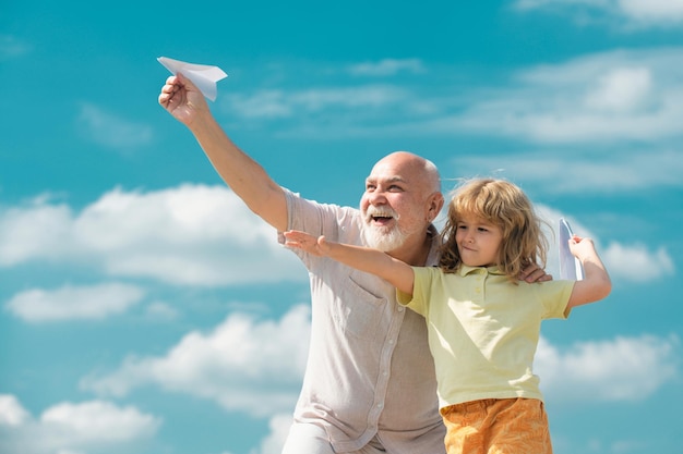 Nonno e figlio che giocano con l'aereo di carta sullo sfondo del cielo estivo bambino ragazzo con sogni di