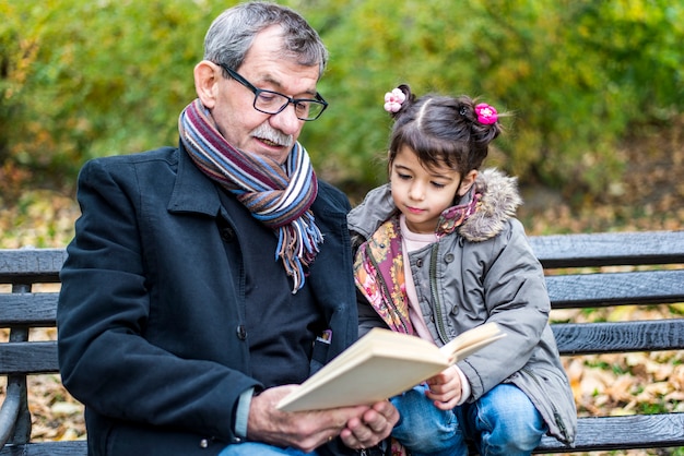 Nonno e nipote che leggono un libro nel parco di autunno