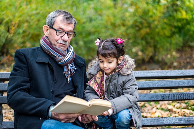 Nonno e nipote che leggono un libro nel parco di autunno