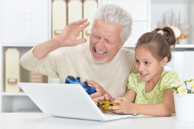 Nonno e nipote emotivi che giocano al gioco per computer con il computer portatile