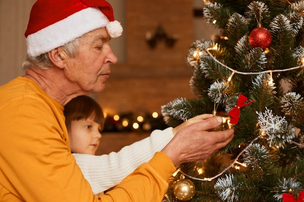 Nonno e nipote nella stanza festiva che decora l'albero di abete, bambina con uomo maturo che celebra insieme il capodanno, buon natale.