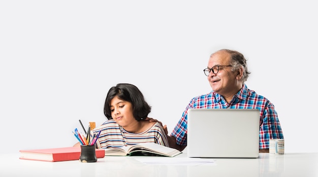 Nonno indiano che insegna alla nipote con libri, matita e laptop, scuola a casa o lezioni