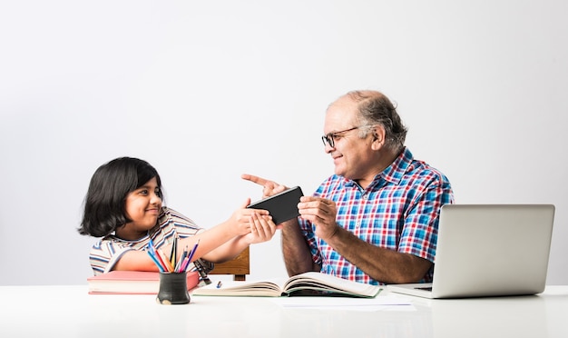 Nonno indiano che insegna alla nipote con libri, matita e laptop, scuola a casa o lezioni