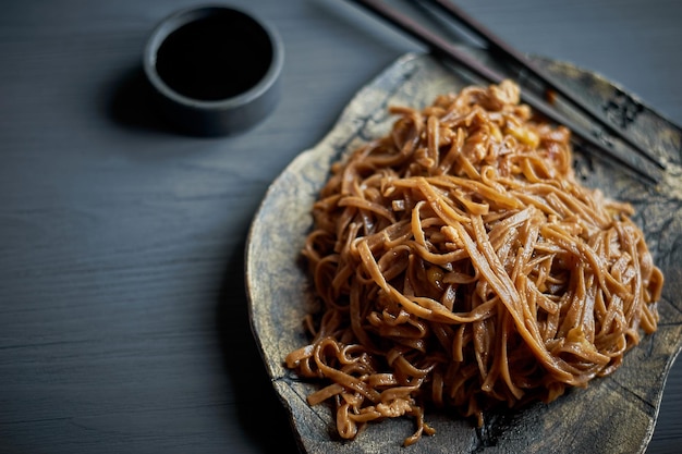 Noodle di grano saraceno con salsa teriakiPiatto asiatico con bastoncini di legno su un piatto di argilla e uno sfondo grigio