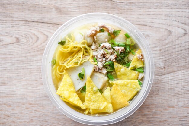 Noodles polpette di maiale polpette di pesce e carne di maiale macinata con wonton croccanti e verdure in una ciotola di plastica sul tavolo di legno vista dall'alto concetto di consegna di cibo tailandese e cinese asiatico