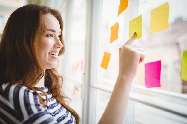 Note adesive commoventi della donna di affari felice sulla finestra in ufficio creativo