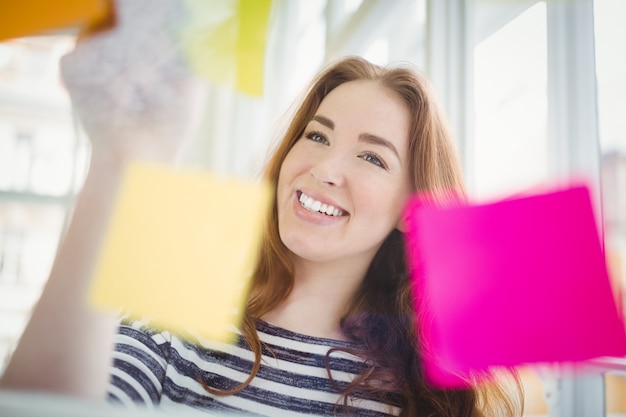 Note adesive commoventi sorridenti della donna di affari in ufficio creativo