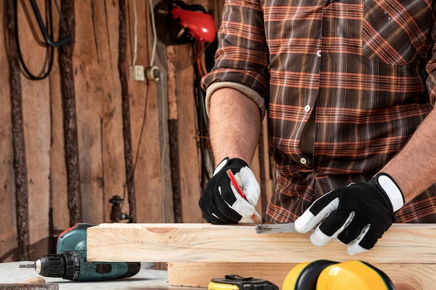 Note dell'uomo del carpentiere con una matita sui segni del bordo per il taglio, mani maschii con un primo piano della matita su un bordo di legno. carpenteria