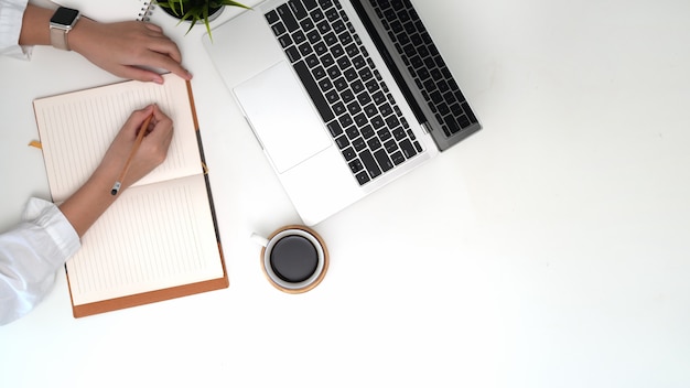 Note di scrittura della donna lavoratrice di vista superiore sul taccuino sull&#39;area di lavoro dell&#39;ufficio