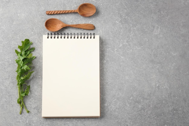 Notebook con cucchiai di legno e rucola su sfondo grigio Corsi di perfezionamento di cucina