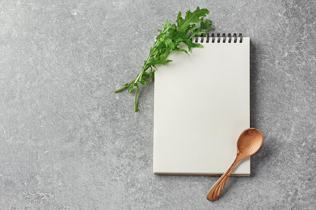 Notebook con cucchiaio di legno e rucola su sfondo grigio Corsi di perfezionamento di cucina