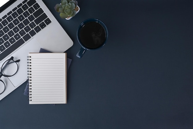 Notebook per computer portatile e tazza di caffè su sfondo blu scuro Spazio per la copia della vista dall'alto