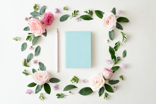 Notebook piatto su sfondo bianco con foglie estive, fiori e altri articoli di cancelleria in stile trendy