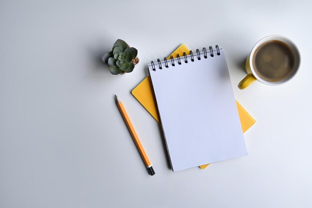 Notebook tazza di caffè matita e pianta succulenta su tavolo bianco Posa piatta