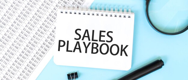 Notepad bianco e lente di ingrandimento sulla documentazione finanziaria Testo SALES PLAYBOOK Concetto aziendale