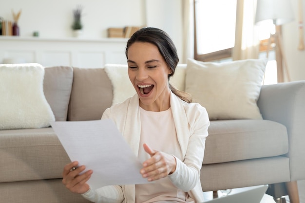 Notizie perfette Eccitata giovane donna adulta felice che urla di gioia tenendo in mano una lettera di carta felicissima studentessa universitaria adolescente sorpresa che legge il documento ufficiale della vincita della borsa di studio o dell'ottenimento della borsa di studio