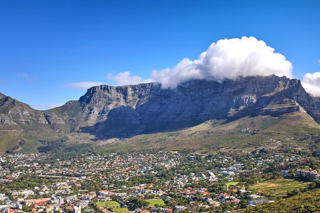 Nubi cumuliformi che si formano sopra la montagna di Lions Head contro un cielo blu con copyspace Paesaggio panoramico di montagne verdi con vegetazione che circonda una città urbana a Cape Town in Sud Africa